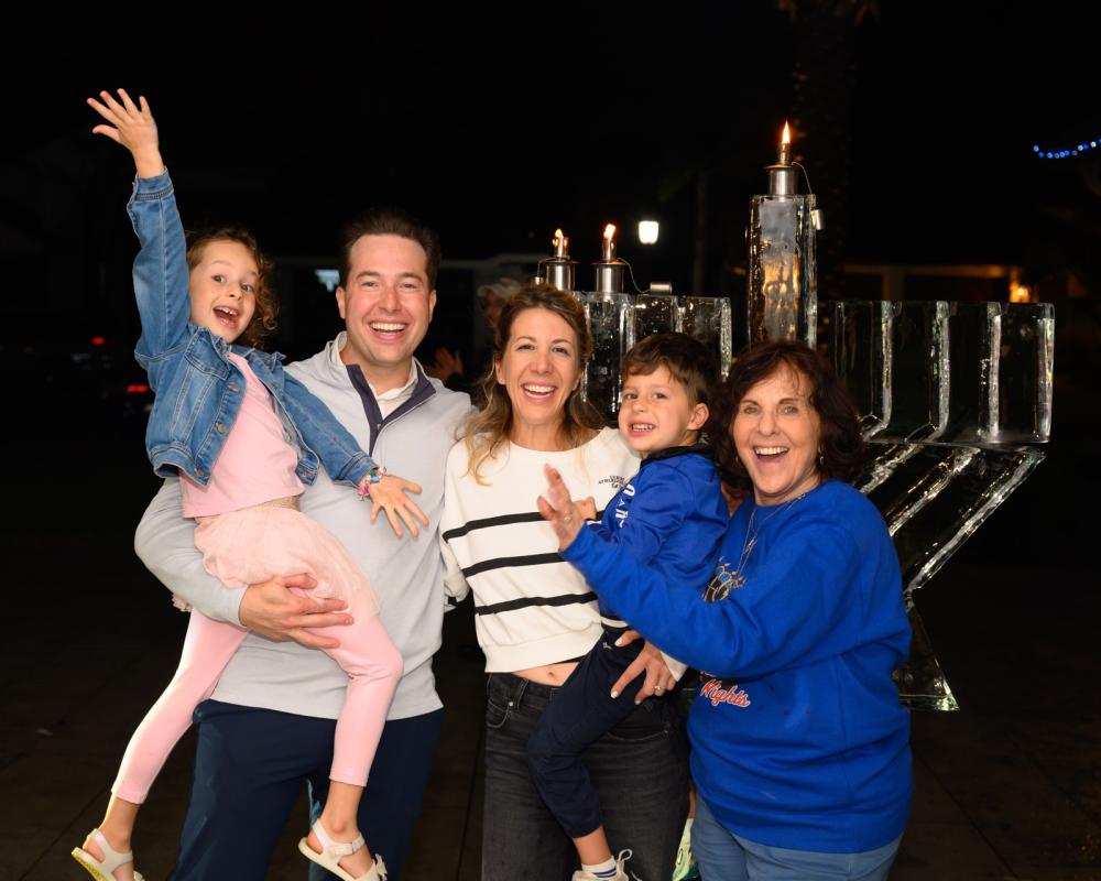 A smiling family celebrating beside the ice menorah